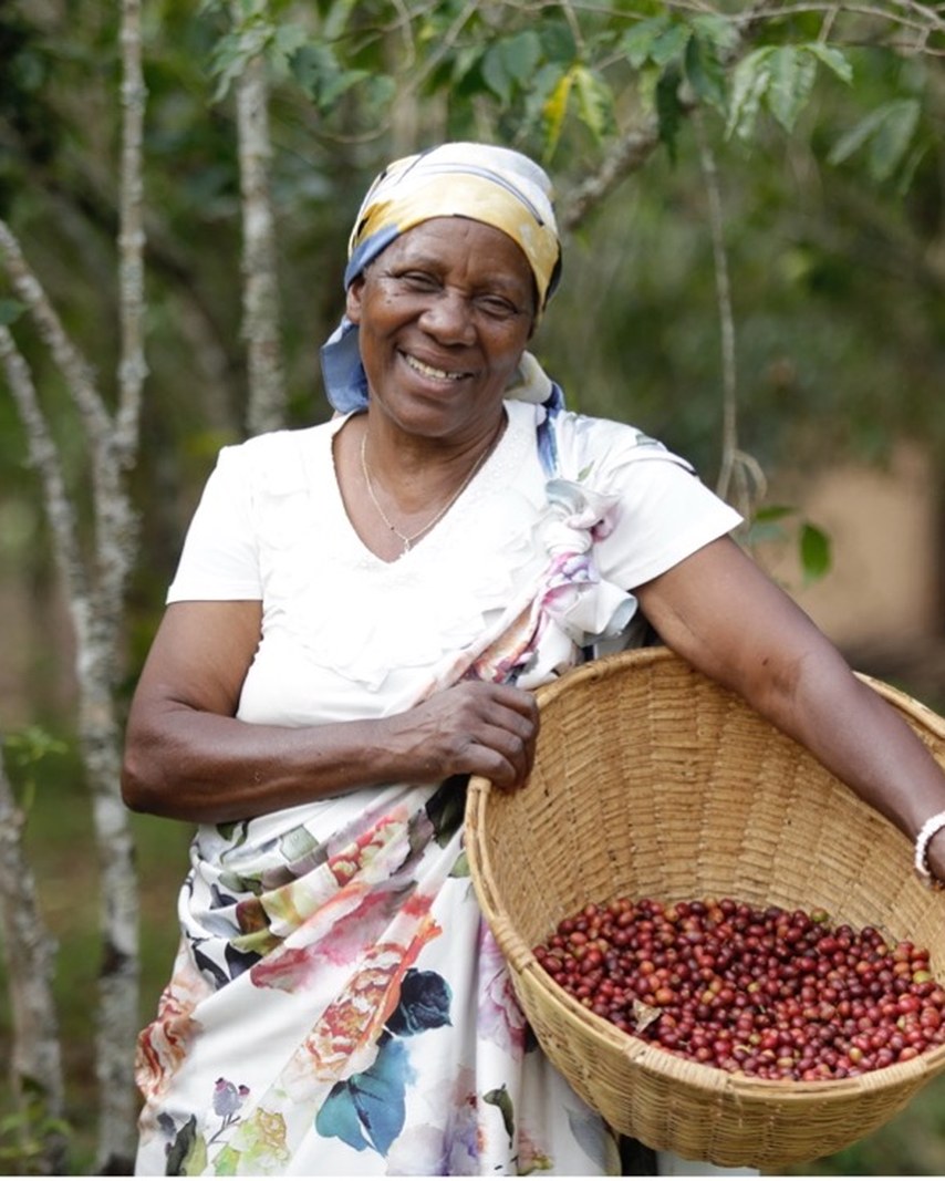 Pauline Ntaconkurikira smiling, holding a basket of ripe coffee cherries in Burundi