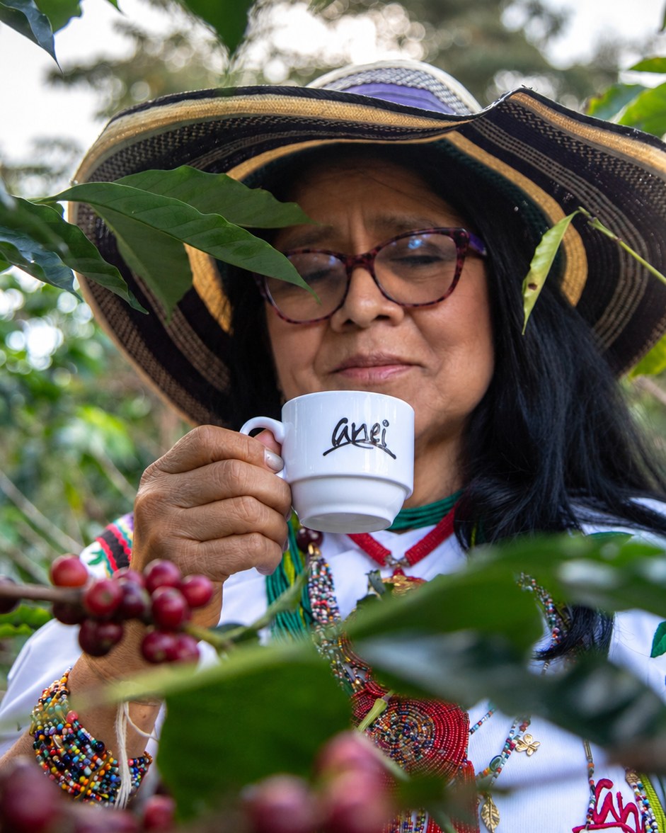 Aurora tasting coffee from an ANEI cup beside ripe coffee cherries